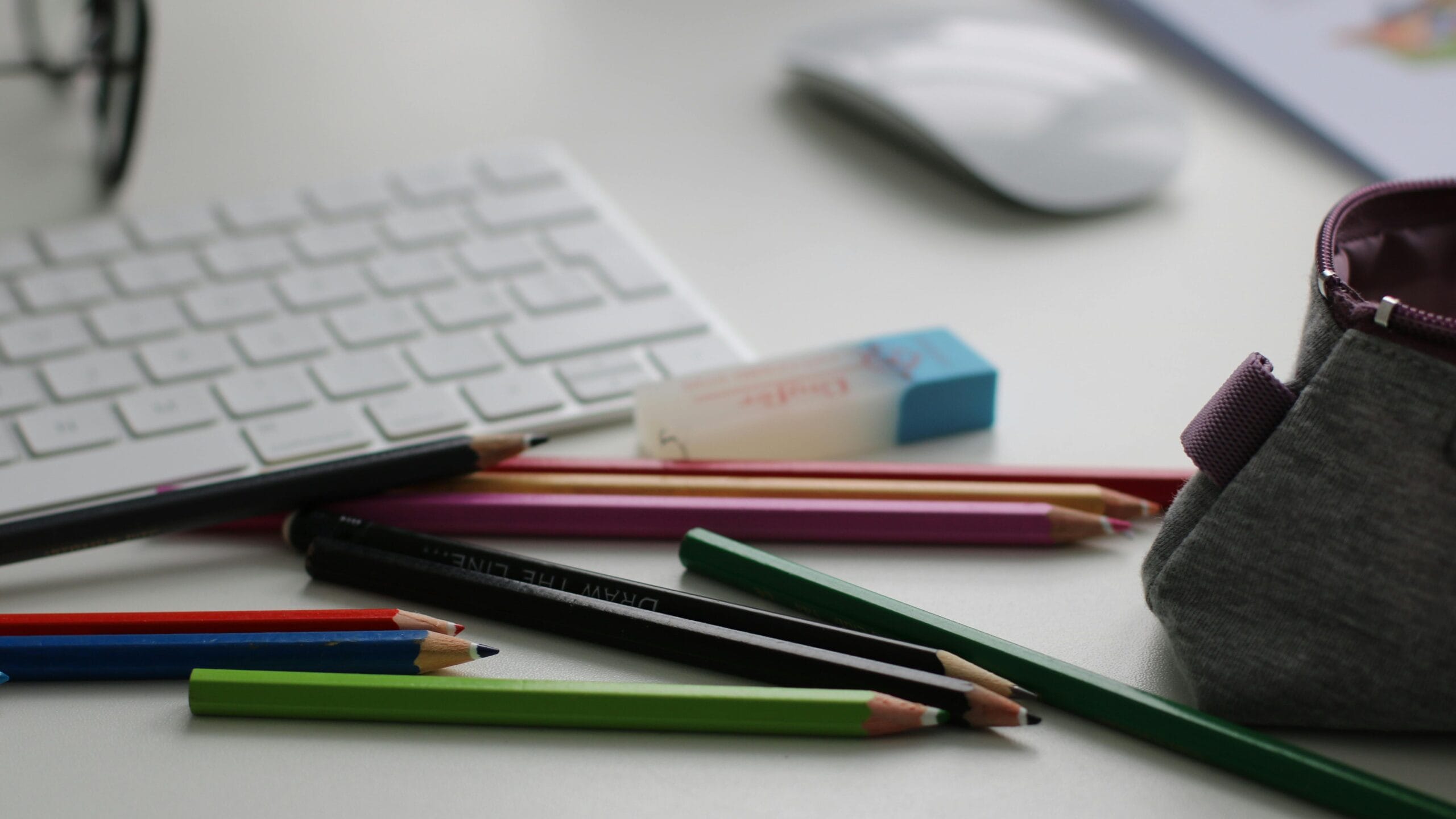 Color pencils and office supplies scattered on a white desk with keyboard and mouse.